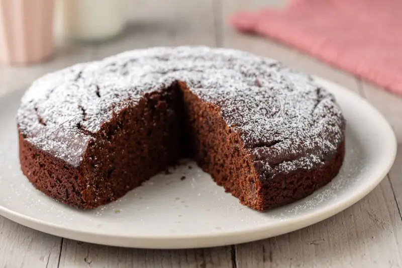 Una fetta è stata tolta da una torta al cioccolato morbida, cosparsa di zucchero a velo.