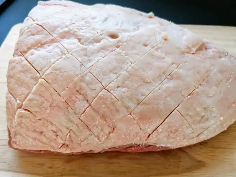 Un pezzo di picanha alla griglia, con la sua copertura di grasso incisa a rombi, pronto per essere cotto su un tagliere di legno.