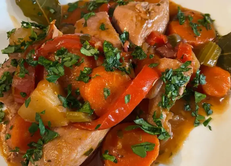 Un saporito spezzatino di pollo con carote, peperoni rossi e prezzemolo tritato, servito in un piatto bianco.