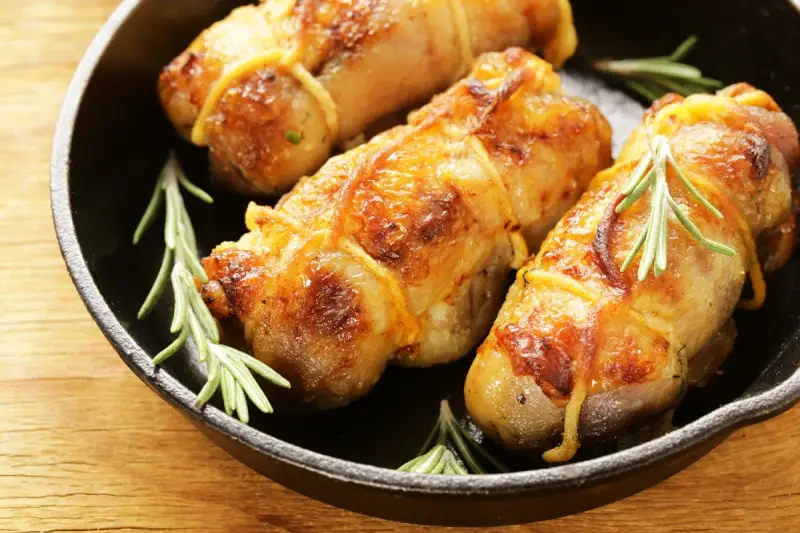 Involtini di pollo in padella, dorati e succulenti, con rametti di rosmarino fresco.